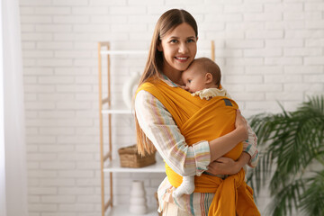 Young happy mother with little baby in sling at home