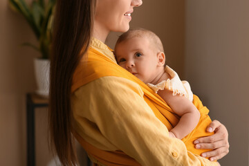 Young mother with her baby in sling at home