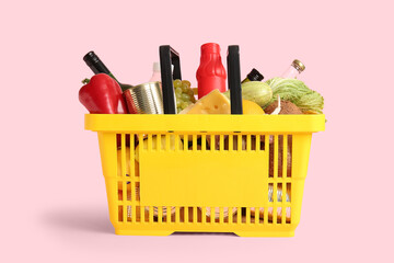 Yellow shopping basket full of different fresh products and bell pepper on pink background