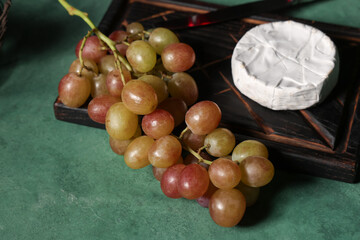 Wooden board with sweet ripe grapes and camembert cheese on green background