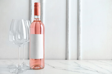 Bottle of pink wine and empty glasses on table against white background
