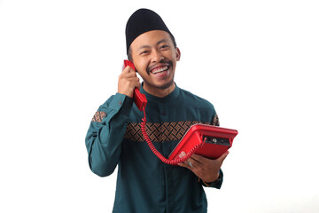 Cheerful Asian Muslim man talking on a landline phone, isolated on a white background