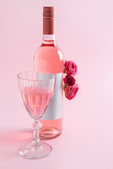 Glass and bottle of pink wine with roses on pink background