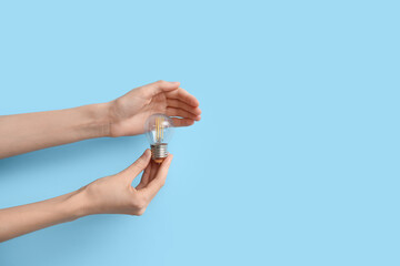 Female hands with round light bulb on blue background