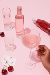 Woman holding pink sparkling cocktail with cherries and playing cards on pink background