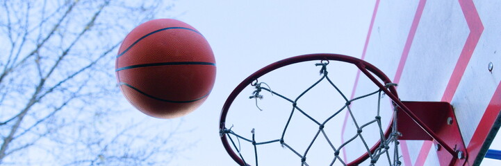 A basketball flies into a basket on a sports court outside.   Vertical shot