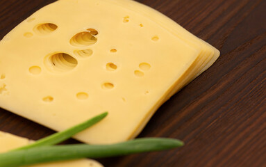 Slices of semi-hard maasdam cheese lying on a wooden kitchen board.