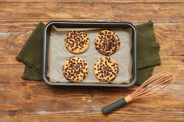 Baking tray with cookies on parchment paper, whisk and towels on wooden background. Top view