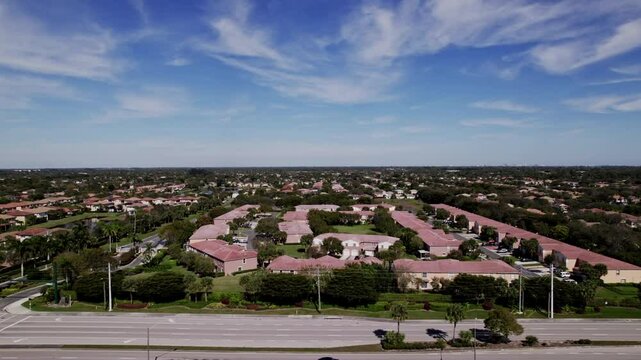 Aerial: West Palm Beach residential zone during the day with a road and blue sky, push in drone shot, USA
