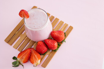Top view of strawberry smoothie in a glass cup next to scattered strawberries on a light colored background. Refreshing natural drink