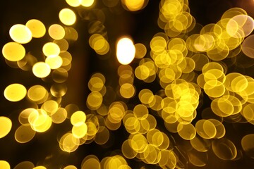 Blurred view of golden lights on dark background, bokeh effect