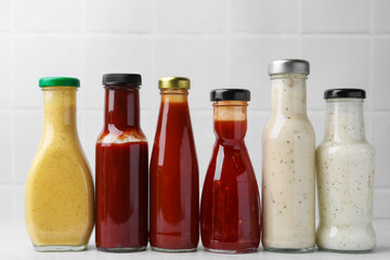 Tasty sauces in glass bottles on white table, closeup
