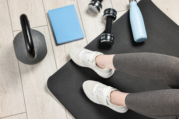 Woman with gym equipment and planner on floor indoors, top view