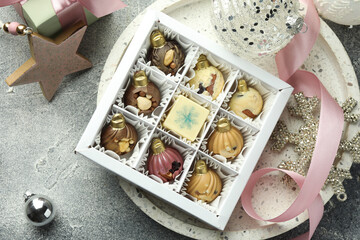 Box with tasty sweets in shape of baubles and Christmas decor on grey background, flat lay