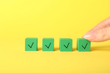 Woman taking green cube with check mark on yellow background, closeup