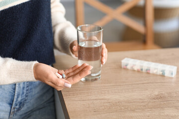 Woman taking medicine in kitchen. Closeup