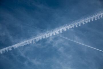 Crossed airplane contrails in a blue sky with wispy clouds. Jet condensation trails forming intersecting lines, symbolizing travel, connection, and motion © Maciej Bonk
