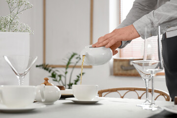 Male waiter pouring tea into cup at table in restaurant, closeup