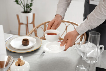 Male waiter putting cup of tea on table in restaurant, closeup