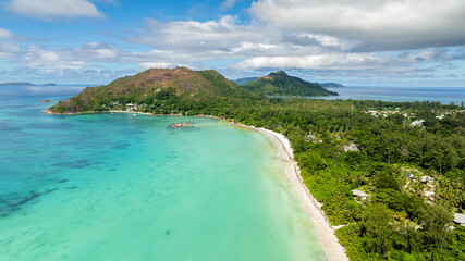 A sweeping curved coastline with green hills, a tranquil turquoise bay, and soft white sands. Praslin, Seychelles.