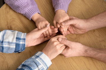 Couple with adopted girl holding hands on table, top view