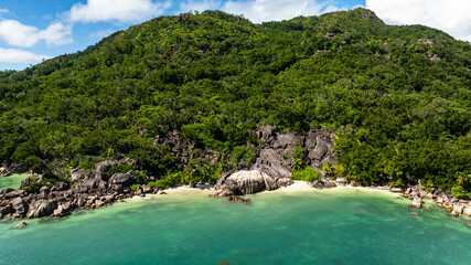 Obraz premium A stunning beach scene featuring clear turquoise waters, large boulders, and dense vegetation along the coastline. Praslin, Seychelles.