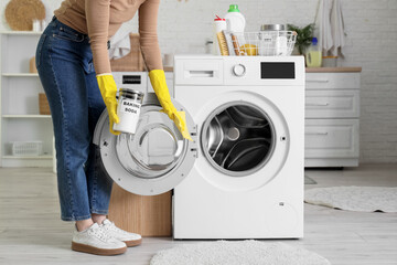 Young woman cleaning washing machine with baking soda in laundry room