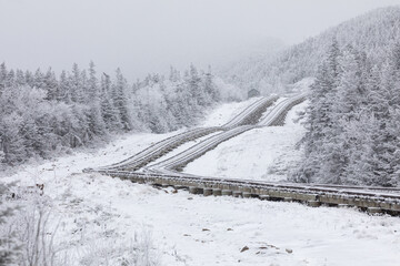 Obraz premium Snow-covered railway tracks wind through the White Mountains of New Hampshire, leading to the summit of Mount Washington. The scenic route passes through forests, creating a stunning winter landscape