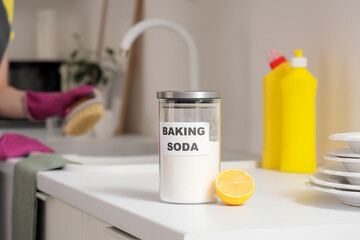 Jar of baking soda with lemon on counter against woman cleaning sink in kitchen, closeup