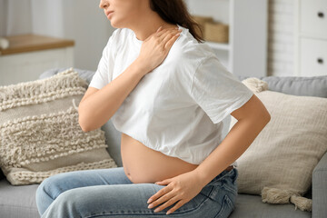 Young pregnant woman suffering from shoulder pain on sofa at home, closeup
