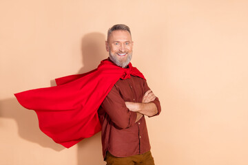 Confident smiling mature man with a stylish red cape standing arms crossed in a beige background exuding charm and positivity.