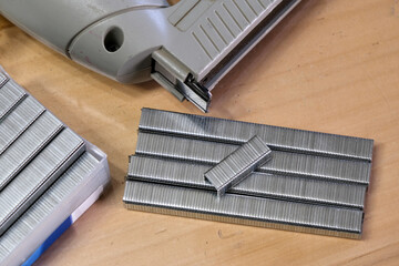 A close-up of a metal staple gun with strips of staples on a wooden surface, emphasizing tools,...
