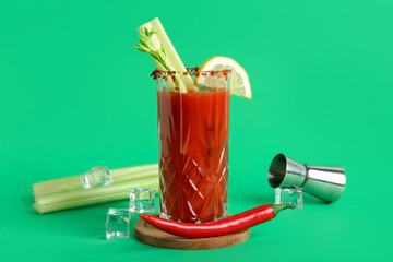Glass of bloody mary cocktail with celery, chili pepper and ice cubes on green background