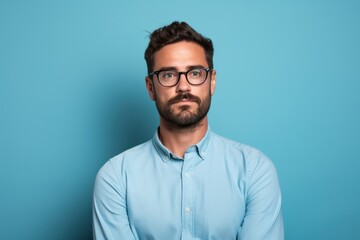 A man with glasses and a beard is standing in front of a blue wall