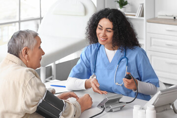 Obraz premium Young African-American doctor measuring senior woman's blood pressure in clinic