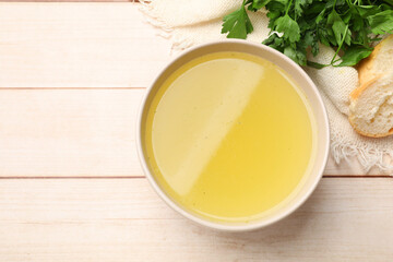 Tasty chicken bouillon in bowl, parsley and bread on wooden table, flat lay. Space for text