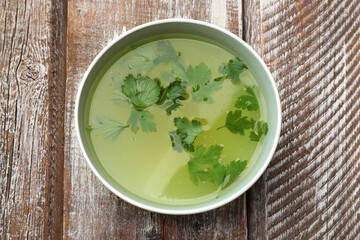 Tasty chicken bouillon in bowl on wooden table, top view