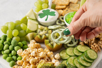 St Patricks day charcuterie board decorated shamrock and clover leaf. Festive holiday appetizer for celebration. Female hands dip cracker to sauce. Close up