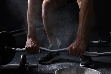 Man with talcum powder on hands training with barbell against black background, closeup