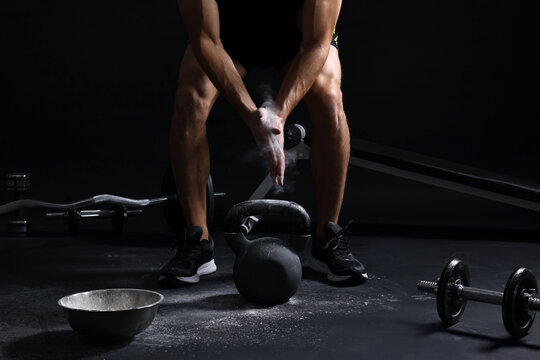 Man clapping hands with talcum powder before training with kettlebell on black background, closeup