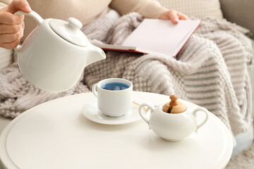 Woman with cup of tasty blue tea reading book at home. Closeup