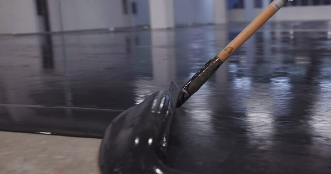 Construction workers applying black epoxy resin on concrete floor