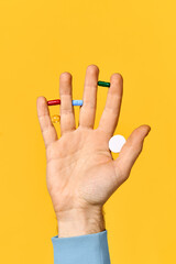 Male hand holding various pills balanced on fingers over yellow background