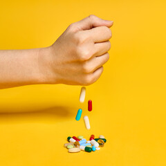 Female hand throws various pills over yellow background