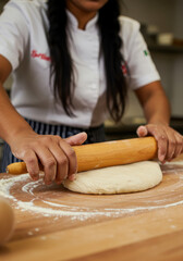 Close up of chef flattening dough with a rolling pin, preparing for baking.