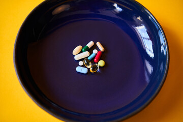 Various pills of different colors and shapes at blue plate over yellow background