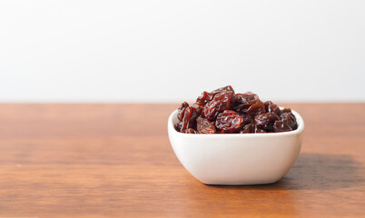 Raisins in white bowl on wooden table background. Dry raisins.