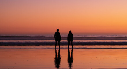 Silhouette of romantic couple standing together on peaceful beach during vivid colorful sunset twilight
