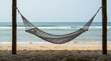 Obraz premium A hammock hangs between two wooden posts under a thatched roof, overlooking gentle ocean waves on a quiet tropical beach.