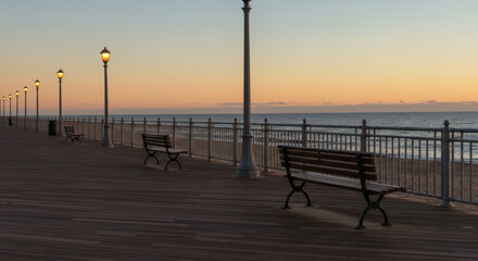 A quiet boardwalk at dusk lined with glowing lampposts, overlooking the calm ocean, evoking peace, nostalgia, and timeless beauty.